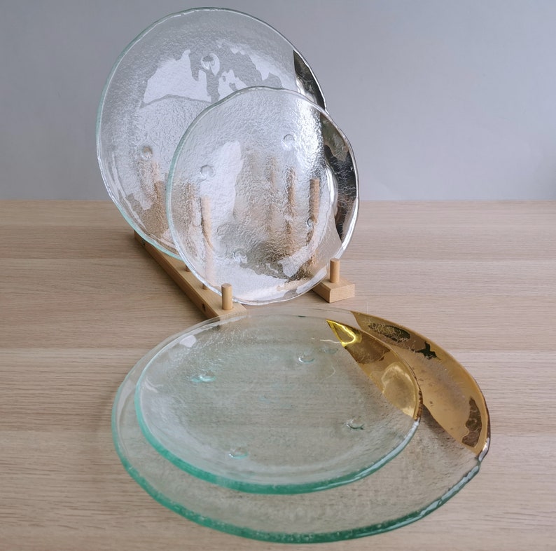 May include: Three clear glass plates with a textured surface, stacked on a wooden stand. The top plate is the largest, and the bottom plate is the smallest. The plates are designed with a subtle pattern that resembles a world map.