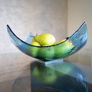 May include: A textured, teal-colored glass bowl, filled with green pears. The bowl has a unique, curved shape and sits on a small, silver-colored base. The pears are ripe and ready to eat, adding a pop of color.