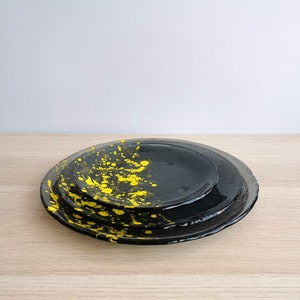 May include: Three black ceramic plates with yellow paint splatters. The plates are stacked on top of each other.