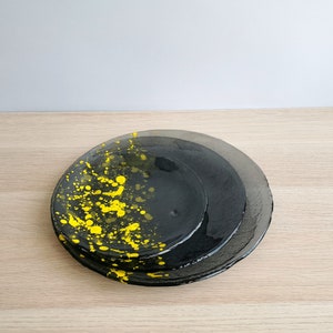 May include: Three black glass plates with a yellow splatter design. The plates are stacked on top of each other.
