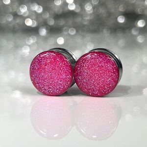 May include: A pair of pink glitter ear gauges with a stainless steel backing.