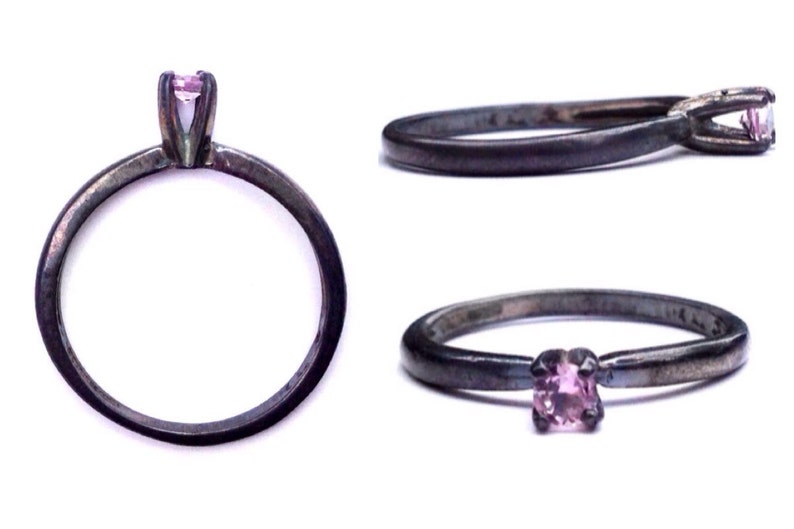 May include: A silver ring with a small pink gemstone set in a prong setting. The ring is oxidized for a darker finish.