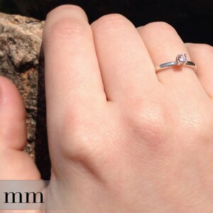 May include: A silver ring with a small, round, pink gemstone. The ring is 3 mm wide.