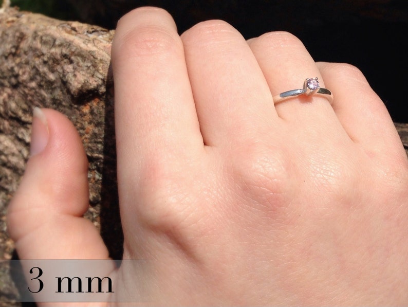 May include: A silver ring with a small, round, pink gemstone. The ring is 3 mm wide.