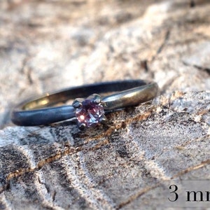 May include: A silver ring with a 3 mm purple gemstone. The ring is oxidized and has a matte finish.