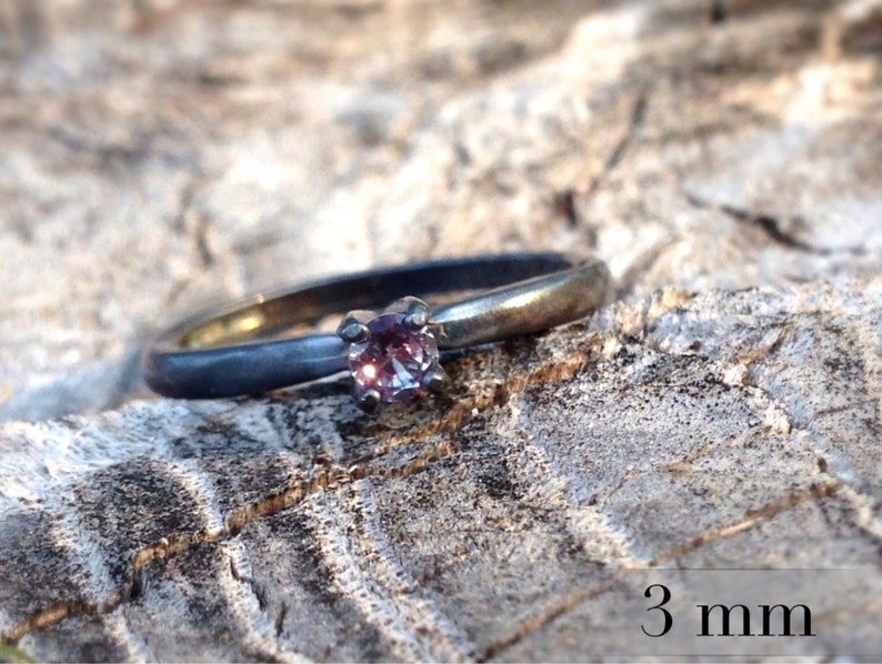 May include: A silver ring with a 3 mm purple gemstone. The ring is oxidized and has a matte finish.