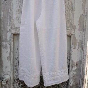 May include: White linen pants with a ruffled hem. The pants have a wide leg and a relaxed fit.
