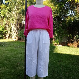 May include: A pink linen top with 3/4 sleeves and a white linen pair of cropped pants with a drawstring waist.