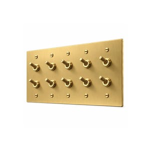 May include: A rectangular brushed brass wall plate featuring ten individual toggle switches arranged in two horizontal rows of five. Each switch has a textured, knurled metal handle, and the plate is secured with five small flathead screws.