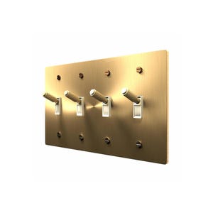 May include: A rectangular brushed brass wall plate featuring four toggle light switches. Each switch has a textured, cylindrical handle and is mounted on a white base. The plate is secured to the wall with eight matching brass screws.
