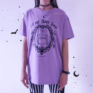 Pode incluir: Camiseta roxa com um gr&aacute;fico preto de um gato em uma moldura com o texto "I'll eat your soul".