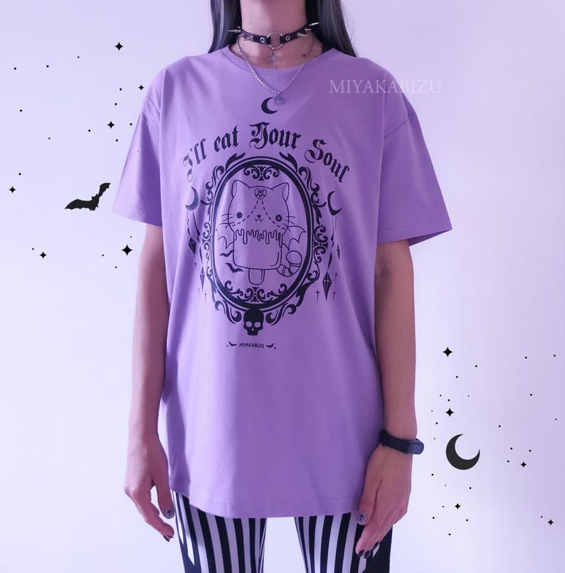 Pode incluir: Camiseta roxa com um gr&aacute;fico preto de um gato em uma moldura com o texto "I'll eat your soul".