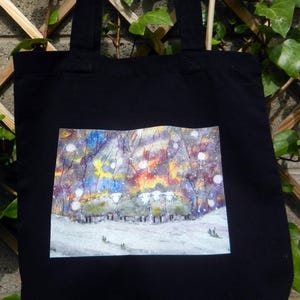 May include: Black tote bag with a rectangular watercolor painting of sheep in a snowy forest scene. The painting features a colorful sky with yellow, blue, and purple hues. The sheep are white with gray wool.