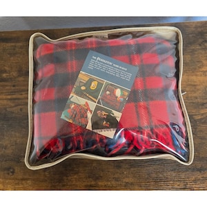 May include: A red and black plaid wool blanket inside a clear plastic carrying case. A product label on the front reads The Pendleton Robe-In-Bag and includes images of the blanket in use, noting dimensions of 52 x 70 inches and 100% virgin wool.
