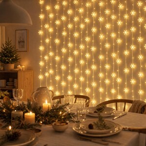 May include: A vertical string light curtain featuring multiple illuminated snowflake-shaped bulbs that emit a warm yellow glow, arranged in parallel lines against a wall to create a festive decorative backdrop for a dining room.