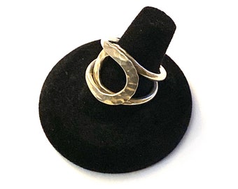 Puede incluir: Un anillo de plata con acabado martillado y un diseño único e entrelazado. El anillo se muestra en un soporte de anillo negro.