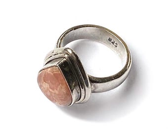 Puede incluir: Un anillo de plata con una gema facetada grande, de color rosa claro. El anillo tiene un engaste cuadrado alrededor de la piedra y una banda sencilla. El metal está estampado con "925".
