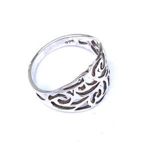 Puede incluir: Un anillo de plata con un dise&ntilde;o calado. El anillo presenta un patr&oacute;n arremolinado y repetitivo. El metal est&aacute; estampado con "925". El anillo est&aacute; sobre un fondo blanco.