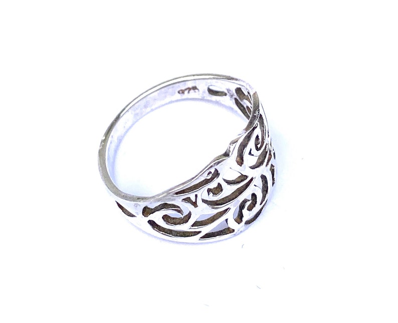 Puede incluir: Un anillo de plata con un dise&ntilde;o calado. El anillo presenta un patr&oacute;n arremolinado y repetitivo. El metal est&aacute; estampado con "925". El anillo est&aacute; sobre un fondo blanco.