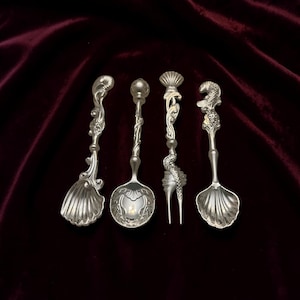 May include: A collection of four ornate silver spoons and a fork, each with unique decorative handles and bowl designs. The spoons and fork are arranged on a dark red velvet surface.