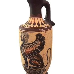 May include: A ceramic vase with a dark brown handle and rim, featuring a beige body with a black and brown illustration of a sphinx. The vase has a rounded base and a narrow neck, showcasing ancient Greek art.