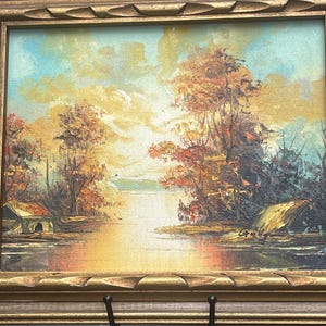 May include: An oil painting in a gold frame depicting a landscape with a river, trees in autumn colors, and small structures on the banks. The sky is filled with light yellow and blue clouds, and the signature Gilly is visible on the right.