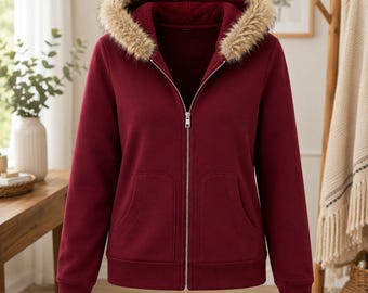 May include: A deep burgundy zip-up hoodie featuring a plush, tan faux fur-lined hood. The garment includes a silver-toned metal zip closure running down the centre, long sleeves with ribbed cuffs, and two front patch pockets for storage.
