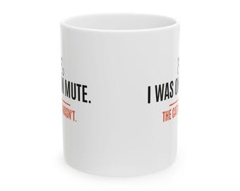 Può includere: Una tazza in ceramica bianca con testo nero che recita I WAS ON MUTE e un testo arancione più piccolo sotto che recita THE CAT WASN'T. Il design include un semplice disegno al tratto di una testa di gatto sopra il testo.