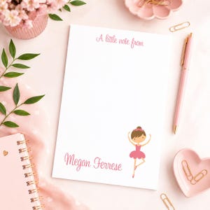 May include: A white rectangular notepad featuring the pink text A little note from at the top and the name Megan Ferrese at the bottom. A cartoon illustration of a ballerina in a pink tutu is positioned next to the name on the notepad.