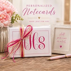 May include: A white box of personalized notecards tied with a pink and gold ribbon. The cards feature pink initials and the text "Personalized Notecards" and "Made Just For You". A pink pen and framed text "Add your name or initials" are also present.