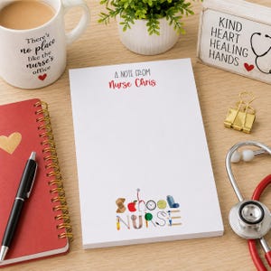 May include: A white notepad with the text "A NOTE FROM Nurse Chris" and "School NURSE". The notepad is on a wooden desk with a red notebook, a pen, a coffee mug, a stethoscope, and a decorative sign.