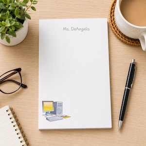 May include: A rectangular white notepad featuring the printed text Ms. DeAngelis at the top and a small colorful illustration of a desktop computer, monitor, keyboard, and mouse at the bottom left corner. The notepad is made of smooth paper.