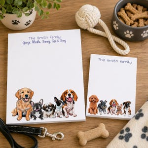 May include: Two white notepads with dog illustrations and the text "The Smith Family". The larger notepad features a golden retriever, French bulldog, and other breeds. A dog leash, toy, and bowl of treats are also present.