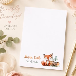 May include: A white personalized notepad with a watercolor illustration of a sleeping fox. The notepad includes the text "Beautifully Personalized", "Made Just For You", and a name and grade. A gold pen and floral accents are in the background.