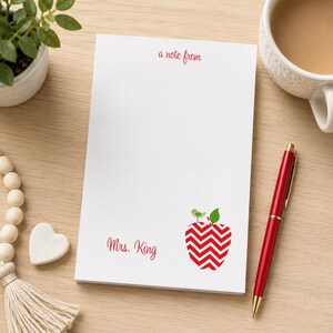 May include: A white rectangular notepad featuring the red text a note from at the top and the name Mrs. King in red script at the bottom left. A red and white chevron patterned apple graphic with a small green bird sits on the bottom right.