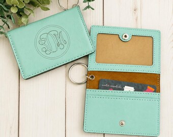 May include: Two mint green leatherette card holders with silver key rings. One is closed, showing a circular monogram with the letters SDM. The other is open, revealing a clear ID window, a brown interior, and a card labeled winter essentials.