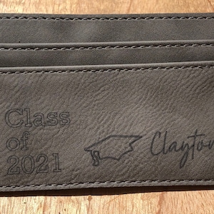 May include: Gray leather card holder with the text "Class of 2021" and a graduation cap graphic. The name "Clayton" is written in cursive below the graphic.