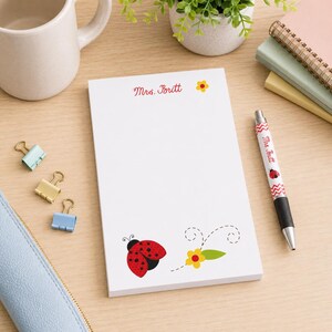 May include: White notepad with a ladybug and flower design. The notepad has the text "Mrs. Britt" in red script. A matching pen with a ladybug and chevron pattern is also visible.