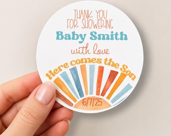 Puede incluir: Una pegatina blanca circular con el texto THANK YOU FOR SHOWERING, Baby Smith, with love y Here comes the Son. El diseño incluye un gráfico de sol con rayos en tonos naranja, azul y rojo, y la fecha 6/7/25 en la parte inferior.