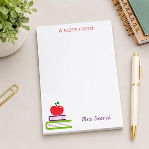 May include: White notepad with the text "A NOTE FROM" in red at the top. The bottom left corner features a stack of books with an apple on top. The name "Mrs. Search" is printed in purple. A gold pen and paper clip are also visible.