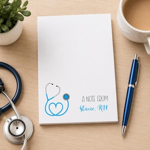 May include: A white rectangular notepad featuring a blue stethoscope graphic shaped like a heart in the bottom left corner. The text reads A NOTE FROM Stacie, RN in black and blue script and sans-serif fonts on the lower right side of the page.