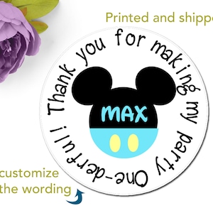 May include: Round white sticker with black Mickey Mouse ears and a blue and yellow face. The text "Thank you for making my party One-derful!" is printed around the image. The name "MAX" is printed in blue on the face.