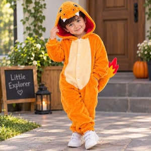 May include: A bright orange plush one-piece jumpsuit featuring a hood with a character face, white teeth, and a red interior. The garment has a cream-colored chest panel, a button-front closure, and a flame-shaped tail attachment on the back.