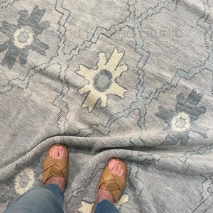 May include: A light gray area rug featuring a repeating geometric pattern of dark gray and cream-colored star-like motifs connected by thin, jagged lines. The rug has a textured, woven surface with a soft, slightly distressed appearance.