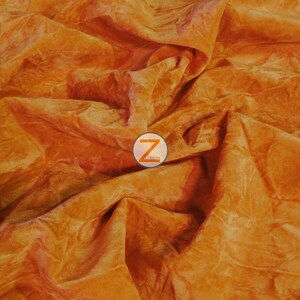 Op de afbeelding: Close-up van een gekreukelde oranje stof met een textuur. De stof voelt zacht en fluweelachtig aan.