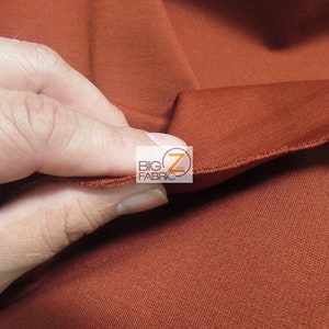 May include: Close-up of a rust-colored fabric with a smooth, slightly textured surface. The fabric is folded over, showing the inside of the fold.