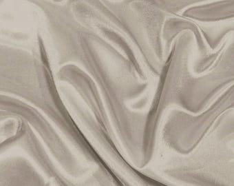 May include: A close-up of a smooth, light beige fabric with soft, flowing folds. The fabric has a subtle sheen and a luxurious feel.