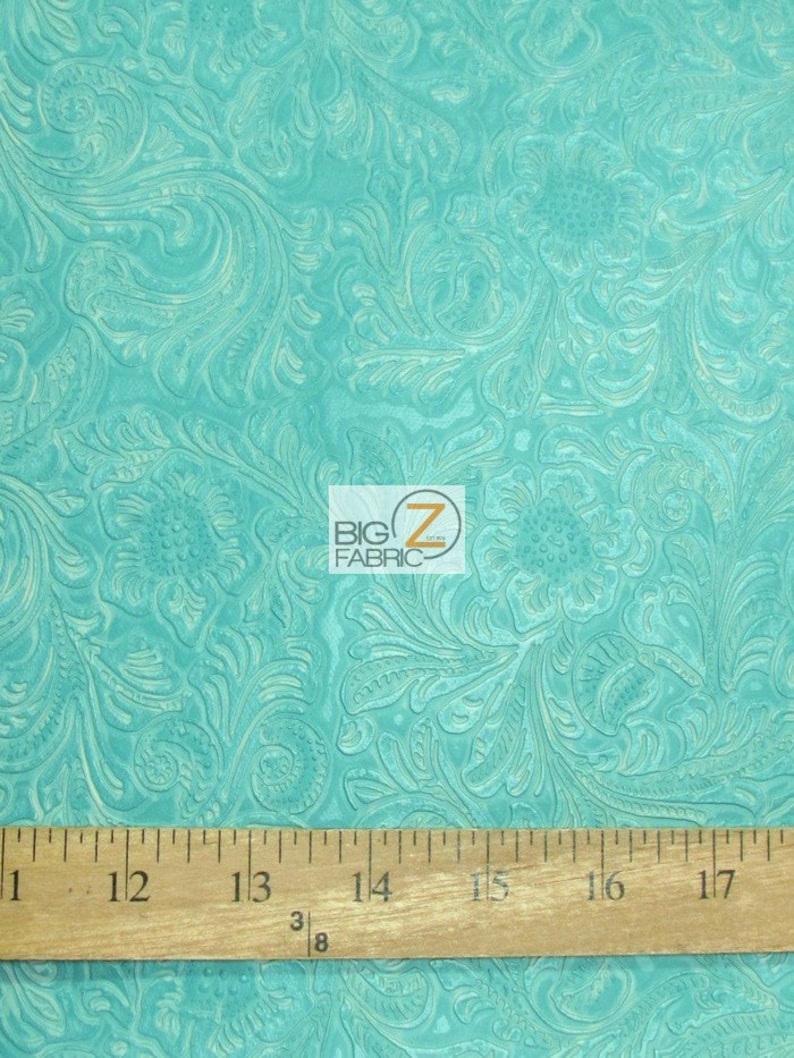May include: Turquoise blue fabric with an embossed floral pattern. The fabric is textured and has a subtle sheen. A ruler is included for scale, showing the fabric is 17 inches wide.