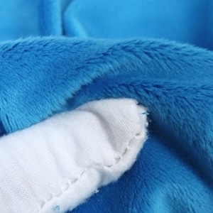 K&ouml;nnte beinhalten: Nahaufnahme eines blauen Pl&uuml;schstoffs mit einem wei&szlig;en, gen&auml;hten Akzent. Das blaue Material hat eine weiche, pelzige Textur. Der wei&szlig;e Akzent hat eine glatte, einfarbige Farbe. Das Bild hebt den Kontrast zwischen den Texturen und Farben hervor.