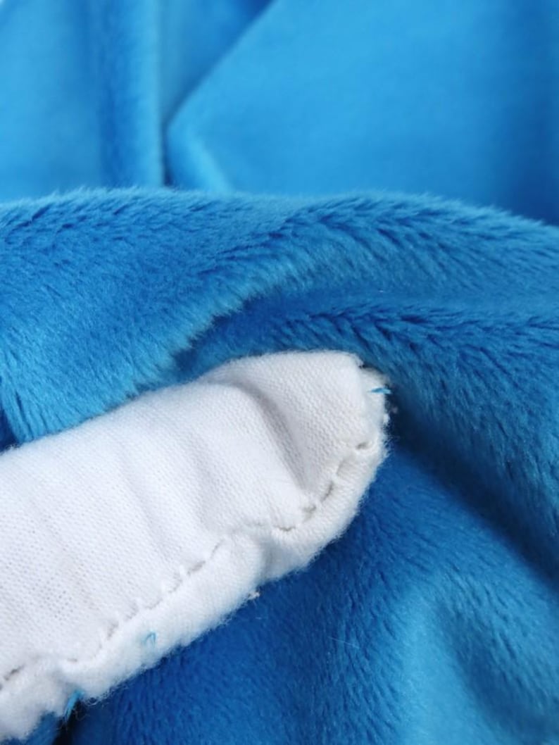K&ouml;nnte beinhalten: Nahaufnahme eines blauen Pl&uuml;schstoffs mit einem wei&szlig;en, gen&auml;hten Akzent. Das blaue Material hat eine weiche, pelzige Textur. Der wei&szlig;e Akzent hat eine glatte, einfarbige Farbe. Das Bild hebt den Kontrast zwischen den Texturen und Farben hervor.
